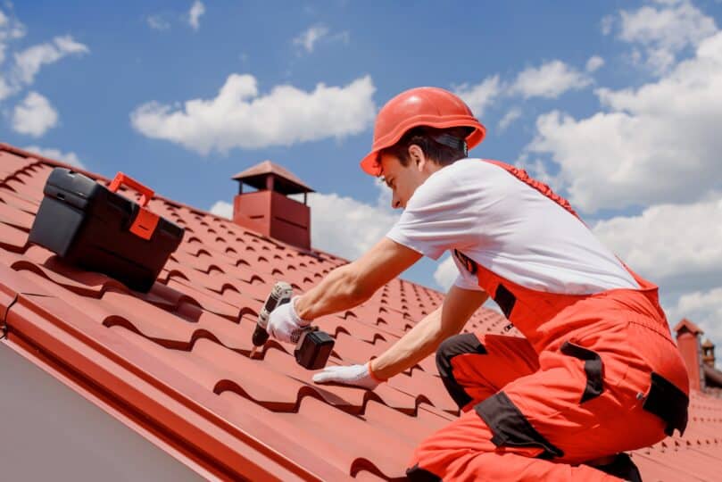 Young,Man,Worker,Master,In,Red,Overall,And,Helmet,Is installing a tile roof